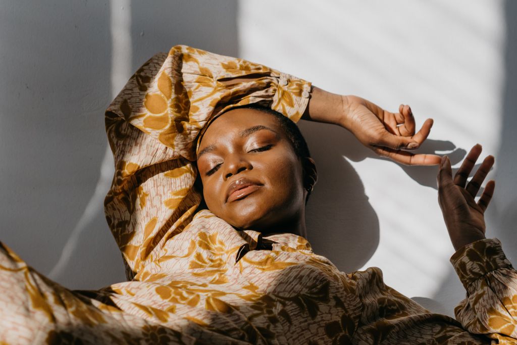 A beautiful woman in a floral dress lying down, basking in soft sunlight indoors.
